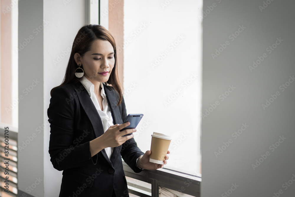Portrait of a confident businesswoman in business suit holding a cup of coffee while using cellphone during break-time in the business building. Business stock photo. Portrait of a confident businesswoman in business suit holding a cup of coffee while using cellphone during break-time in the business building. Business stock photo.