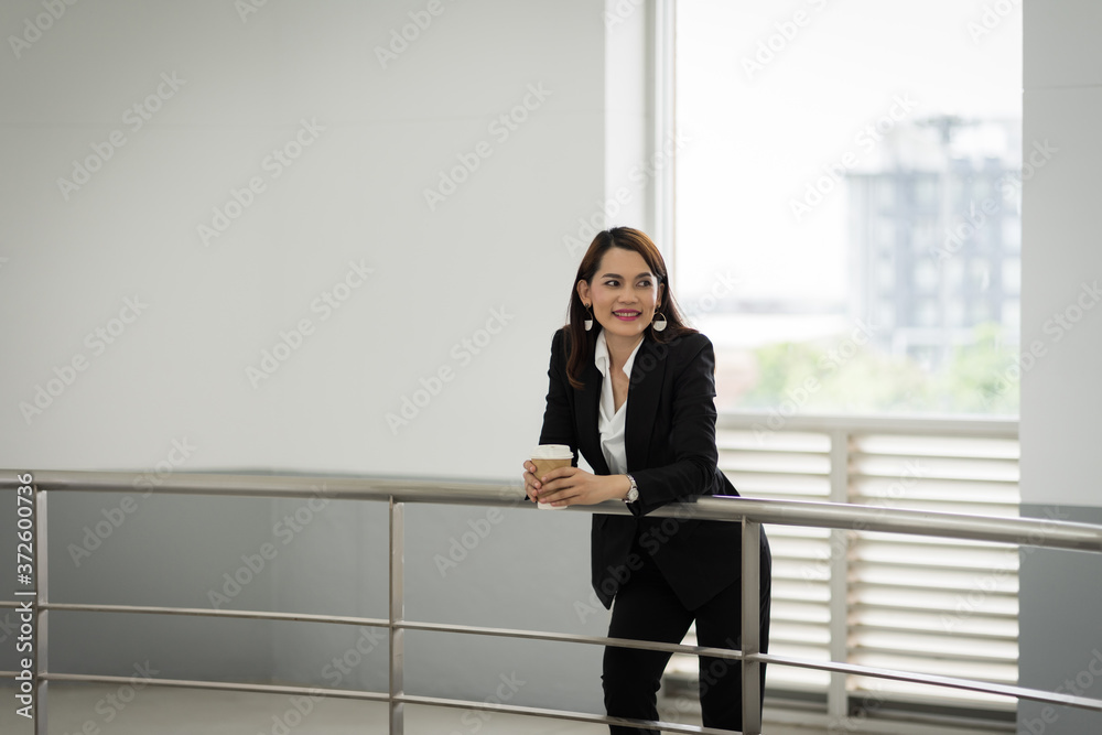 Portrait of a confident businesswoman in business suit holding a cup of coffee while using cellphone during break-time in the business building. Business stock photo. Portrait of a confident businesswoman in business suit holding a cup of coffee while using cellphone during break-time in the business building. Business stock photo.