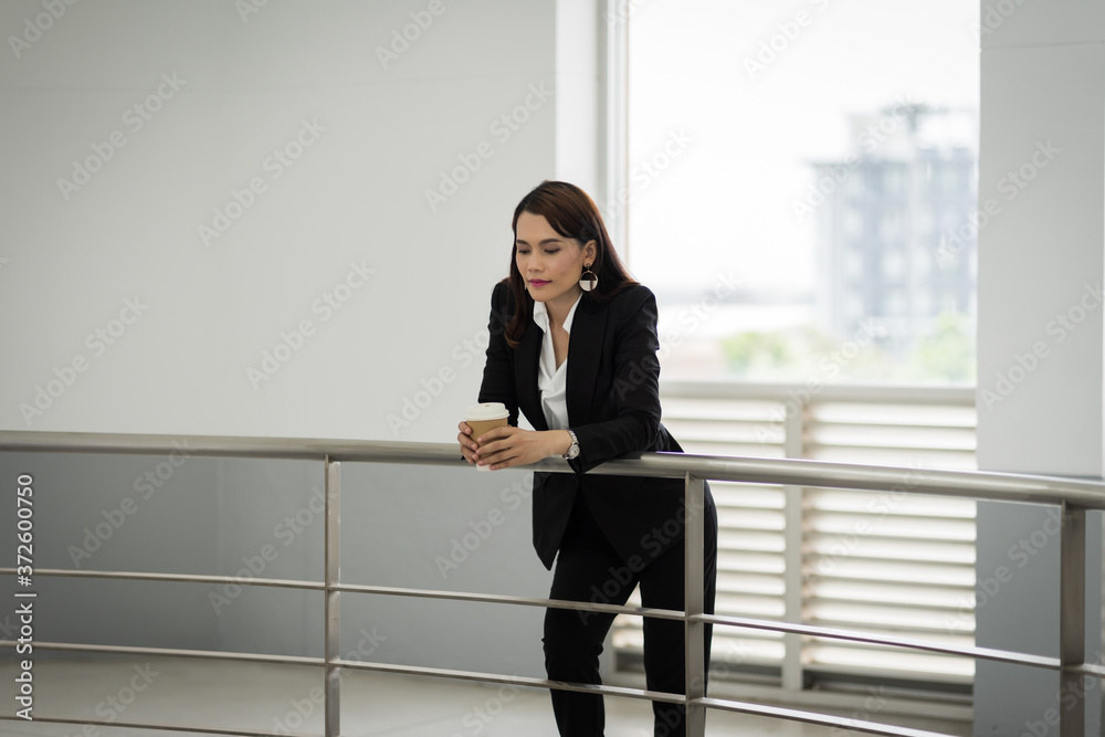 Portrait of a confident businesswoman in business suit holding a cup of coffee while using cellphone during break-time in the business building. Business stock photo. Portrait of a confident businesswoman in business suit holding a cup of coffee while using cellphone during break-time in the business building. Business stock photo.