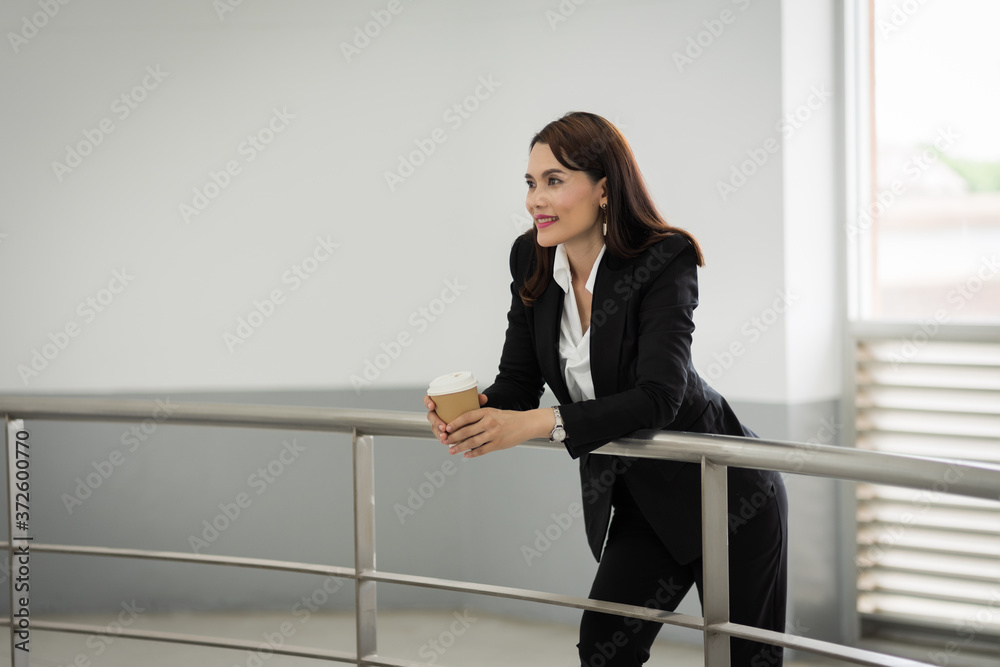 Portrait of a confident businesswoman in business suit holding a cup of coffee while using cellphone during break-time in the business building. Business stock photo. Portrait of a confident businesswoman in business suit holding a cup of coffee while using cellphone during break-time in the business building. Business stock photo.