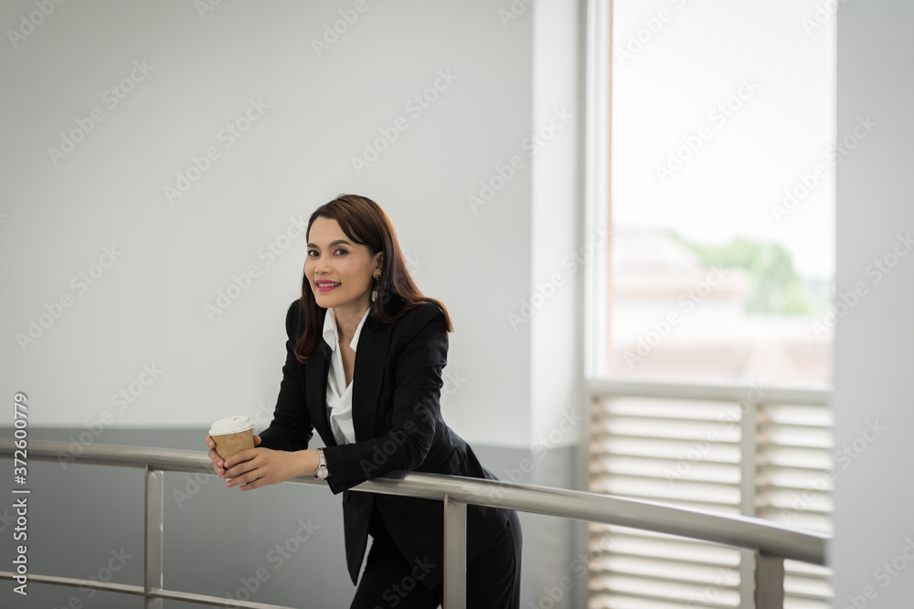 Portrait of a confident businesswoman in business suit holding a cup of coffee while using cellphone during break-time in the business building. Business stock photo. Portrait of a confident businesswoman in business suit holding a cup of coffee while using cellphone during break-time in the business building. Business stock photo.