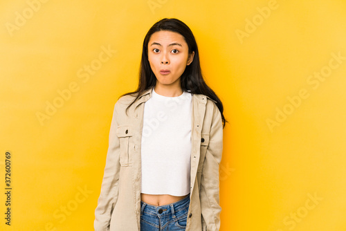 Young chinese woman isolated on a yellow background shrugs shoulders and open eyes confused.