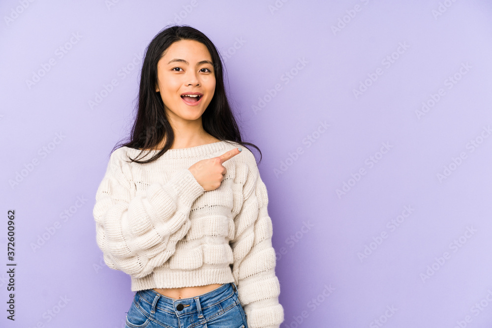 Young chinese woman isolated on a purple background smiling and pointing aside, showing something at blank space. Young chinese woman isolated on a purple background smiling and pointing aside, showing something at blank space.