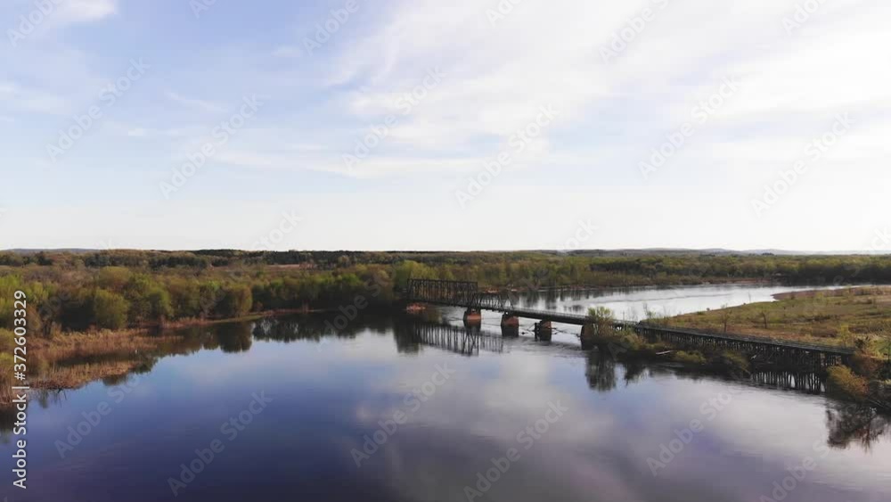 Flying towards a metal bridge across the river. Aerial panoramic view of the drone flying toward isolated old bridge across a calm blue river. Flying towards a metal bridge across the river. Aerial panoramic view of the drone flying toward isolated old bridge across a calm blue river.