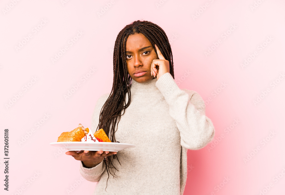 Young african american woman holding a waffle isolated pointing temple with finger, thinking, focused on a task. Young african american woman holding a waffle isolated pointing temple with finger, thinking, focused on a task.