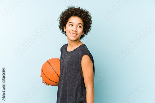 Kid boy playing basketball isolated on blue background looks aside smiling, cheerful and pleasant.
