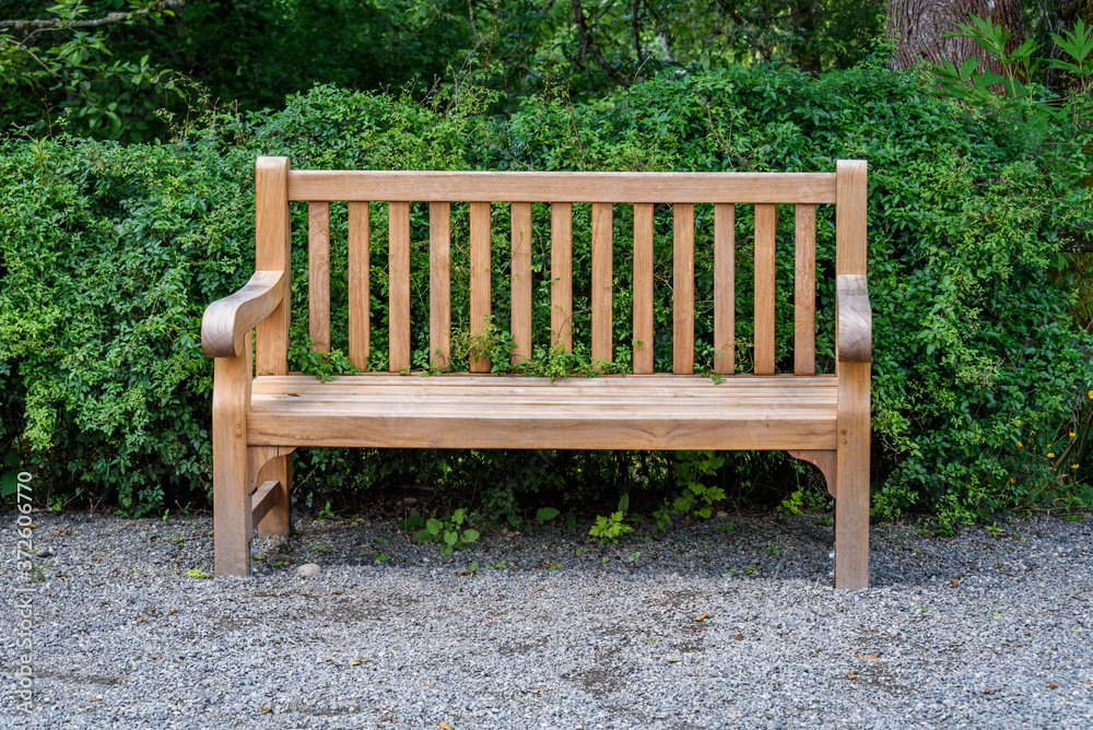 Wooden bench in off a gravel path in a park, ready for a rest stop
