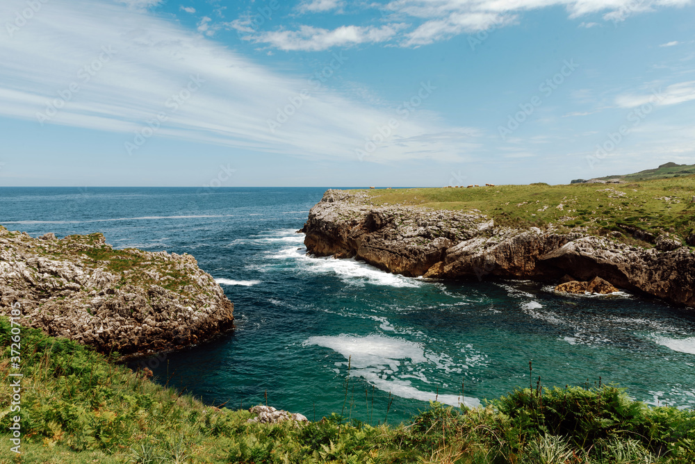 Picturesque view of endless foamy sea near cliffs with uneven surface partially covered with grass under serene sky with clouds Picturesque view of endless foamy sea near cliffs with uneven surface partially covered with grass under serene sky with clouds