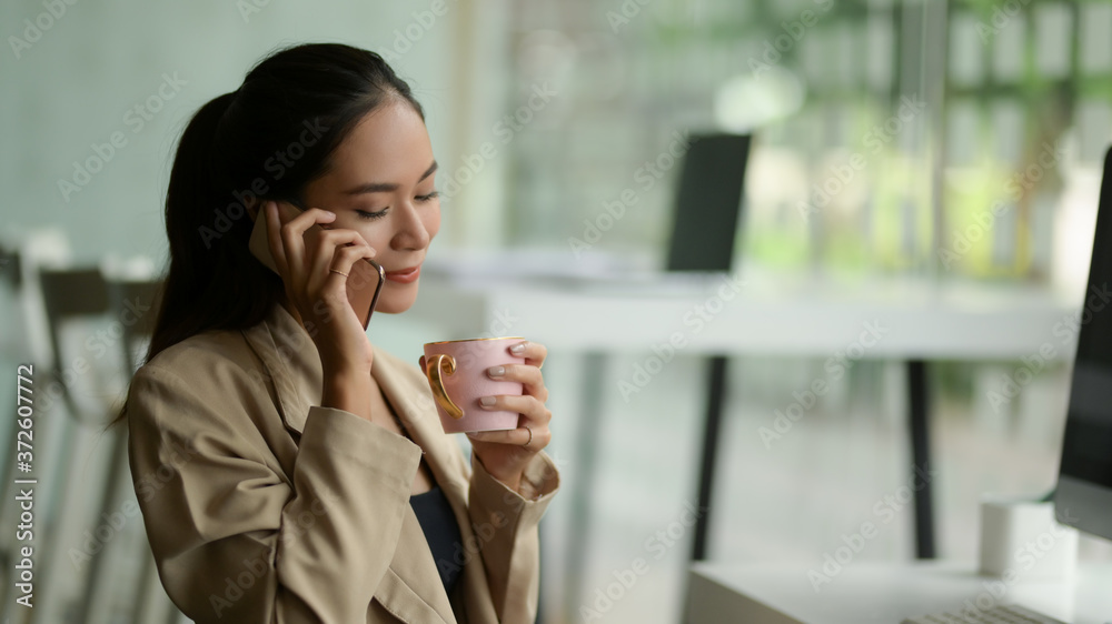 Portrait of female talking on the phone while taking a coffee break in office room