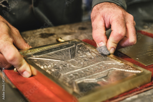 Crop anonymous male jeweler cleaning etching with creative ornament in golden frame using hard piece of fabric in workshop photo