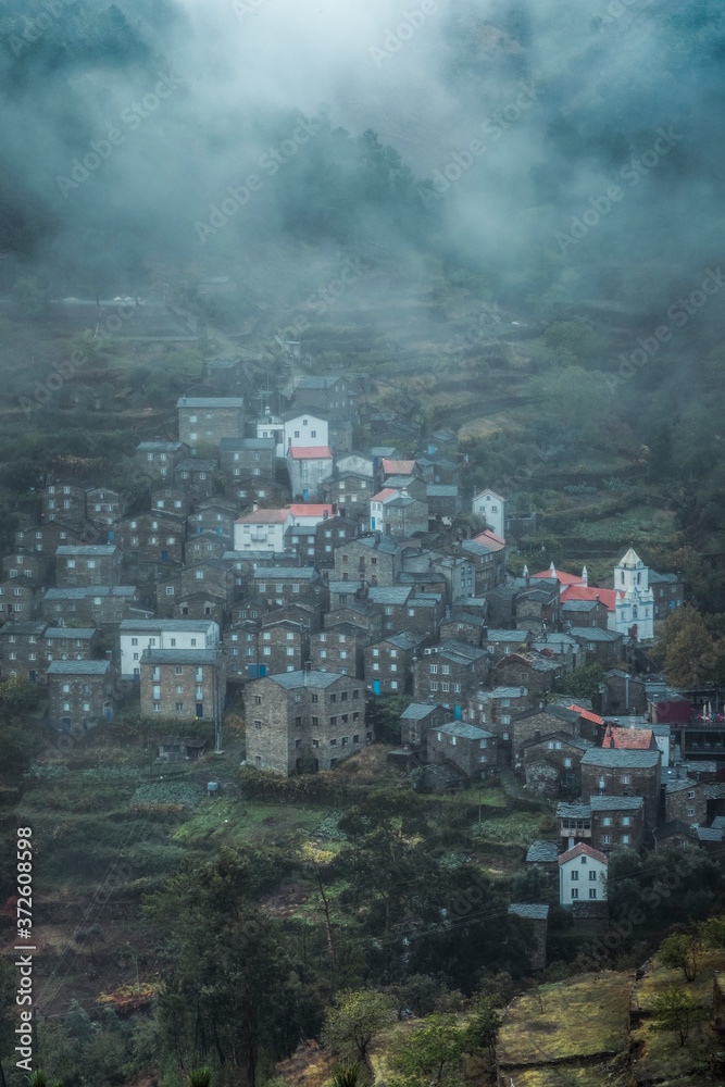 From above of scenery view of village with stone residential buildings surrounded by trees and mountains in foggy weather From above of scenery view of village with stone residential buildings surrounded by trees and mountains in foggy weather