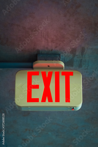 Illuminating rectangular bright red exit sign attached to shabby concrete ceiling in dark room