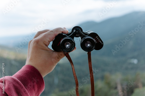 Crop anonymous hiker holding binoculars while observing nature in mountainous terrain in summer day photo