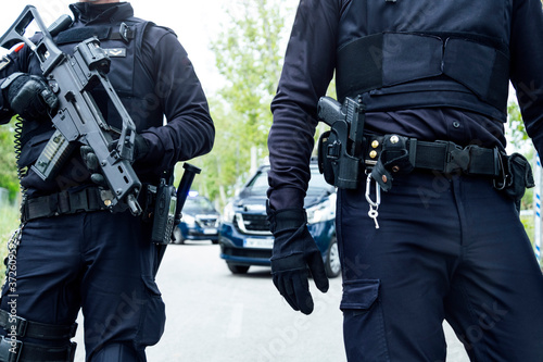 Full body squad of Spanish police officers in protective gears with guns wearing medical masks during patrolling street photo