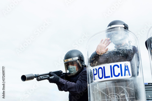 Low angle of swat soldiers in protective uniforms and medical masks armed with assault rifle and riot shield and ready for fight