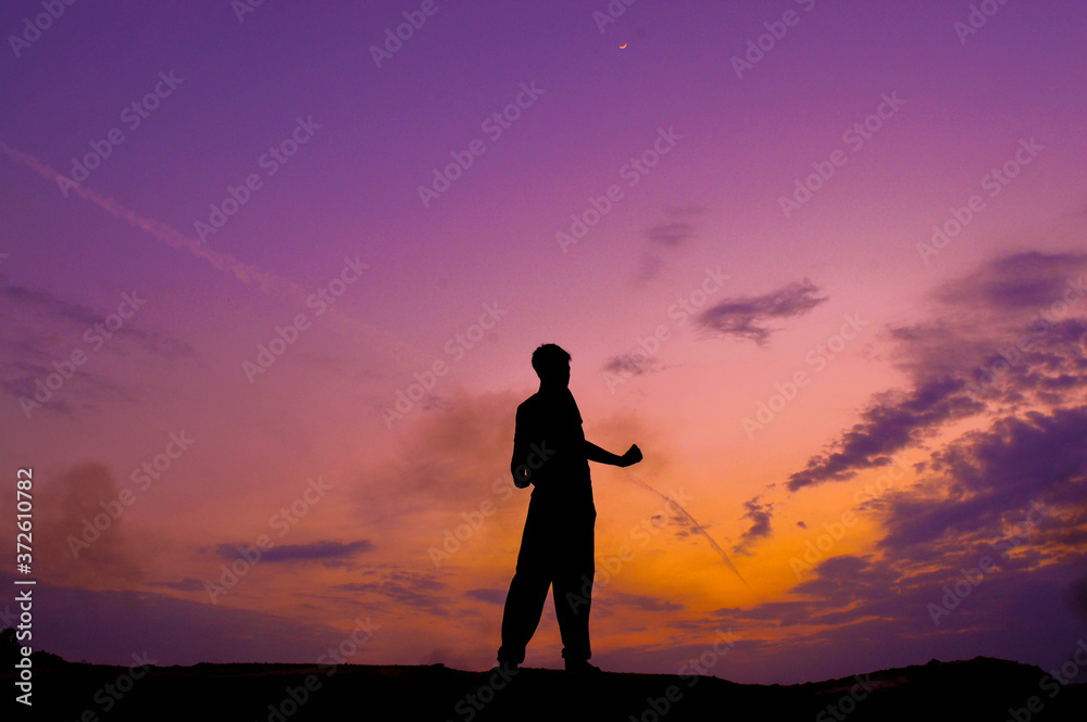 The silhouette of a man standing on a cliff with cool light in the sky.