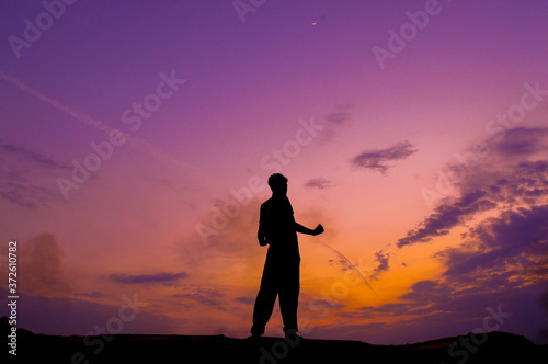 The silhouette of a man standing on a cliff with cool light in the sky.