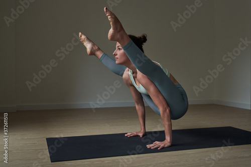 Side view of happy strong young female athlete in leggings balancing on arms while performing Firefly asana during yoga practice photo