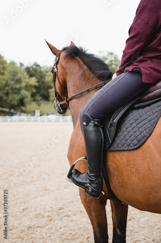Side view of unrecognizable crop female equestrian riding chestnut horse during dressage in park