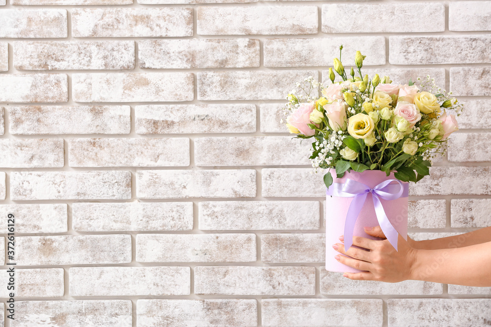 Hands with bouquet of beautiful flowers on brick background