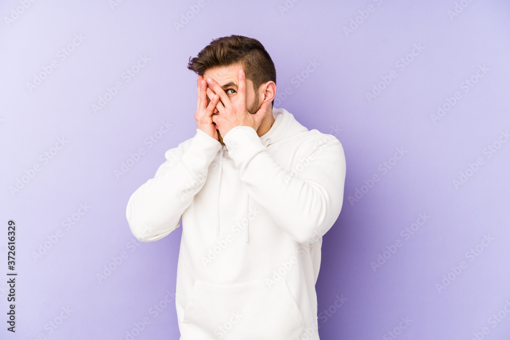 Young caucasian man isolated on purple background blink through fingers frightened and nervous. Young caucasian man isolated on purple background blink through fingers frightened and nervous.
