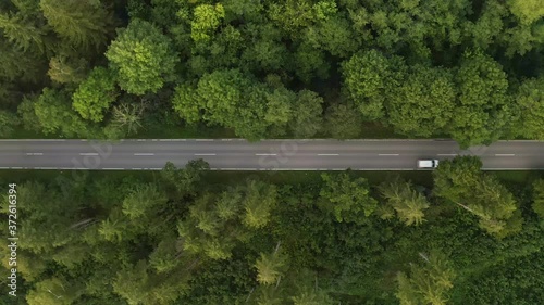 Wallpaper Mural A white passenger car is driving down a street in a green forest, top shot drone footage. Torontodigital.ca