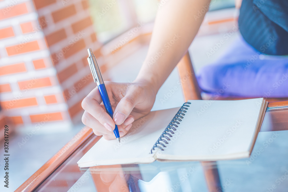 Woman is writing on a notebook with a pen in the office.