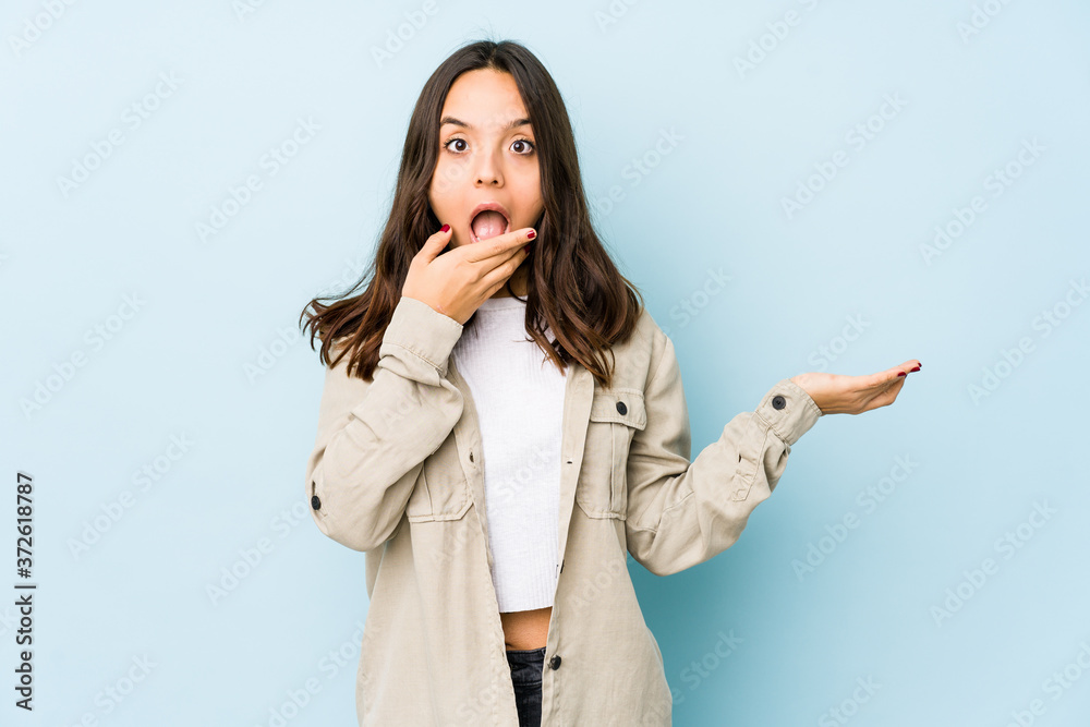Young mixed race hispanic woman isolated holds copy space on a palm, keep hand over cheek. Amazed and delighted. Young mixed race hispanic woman isolated holds copy space on a palm, keep hand over cheek. Amazed and delighted.
