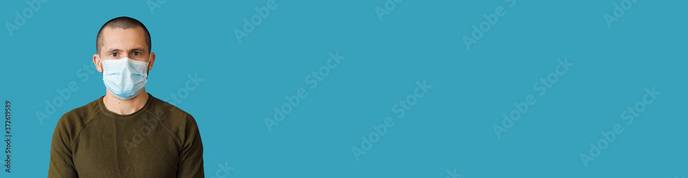 Caucasian man with a white medical mask on face looks at camera on a blue studio wall with free space Caucasian man with a white medical mask on face looks at camera on a blue studio wall with free space