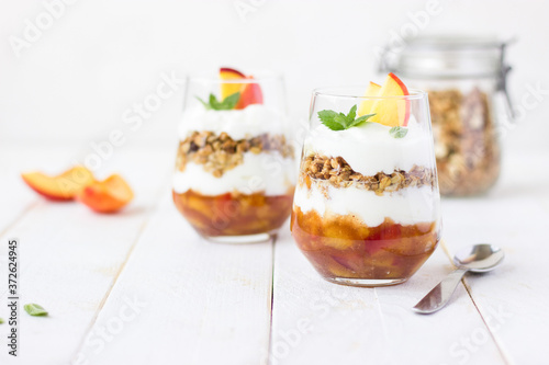 dessert glass of yoghurt, muesli and fruits on a white wooden background. summer, proper nutrition, morning, health, farming, organic food, healthy food concept. free space for text.