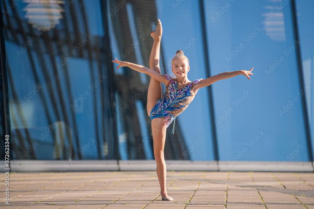 A girl gymnast of school age in a beautiful cross-dress with a black suit performs an exercise without an apparatus.