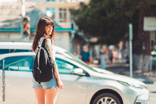 Close up portrait of a woman stands near a road. In the background, a car is driving along the road and traffic light is red. Concept of traffic rules and safety