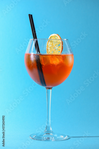 A glass of fruit liqueur in wine glass with a piece of lemon and black plastic straw isolated on pastel blue background.