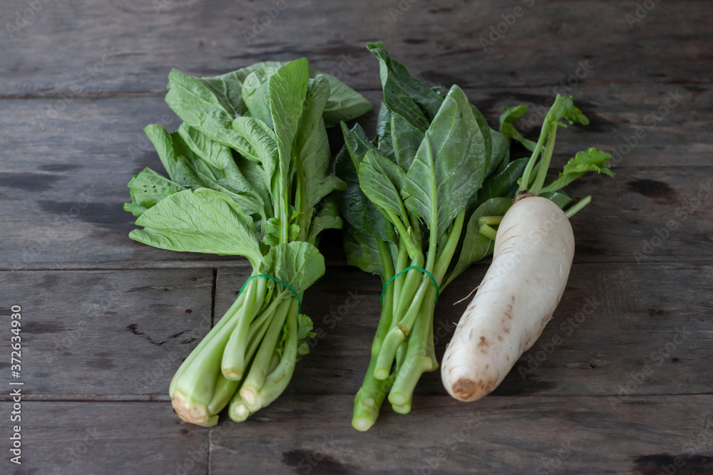Cantonese or bog choy, Collard greens and Radish are placed on the wooden table in the kitchen. Cantonese or bog choy, Collard greens and Radish are placed on the wooden table in the kitchen.