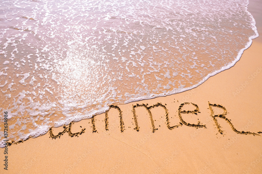 Fototapeta premium Word Summer hand written in the sand with a sea wave. Close up sand texture on beach in summer.