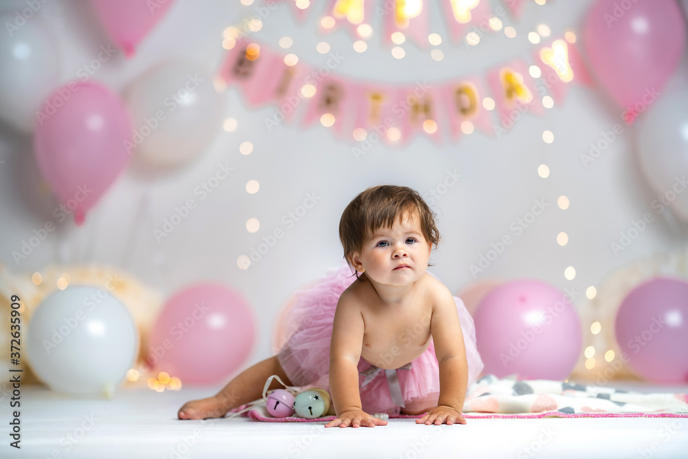 little girl in pink tutu skirt crawls on background with garlands and balloons