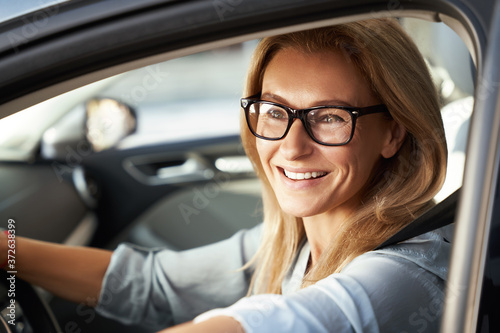 Ready for business trip. Portrait of a beautiful happy caucasian businesswoman wearing glasses sitting in her modern car, looking at camera and smiling