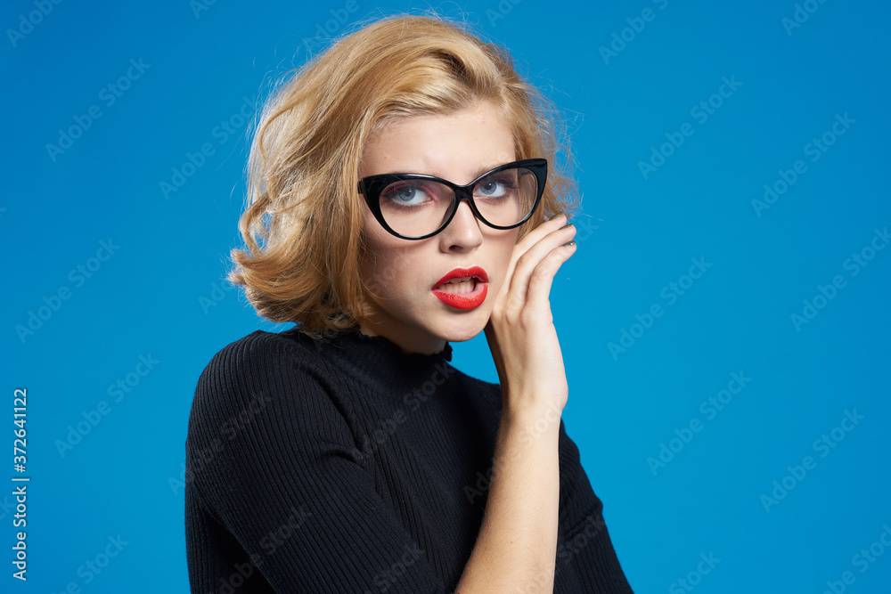 Blonde with short hair red lips glasses black jacket blue isolated background Blonde with short hair red lips glasses black jacket blue isolated background