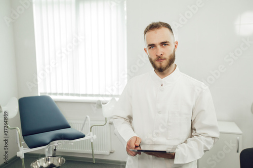 A male gynecologist is alone in the office, holding a tablet and looking at camera. The concept of modern medicine