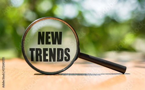 NEW TRENDS text written on magnifying glass. Main trend of changing something. Popular and relevant topics. New trends in business. Recent and latest trend. Evaluation methods.