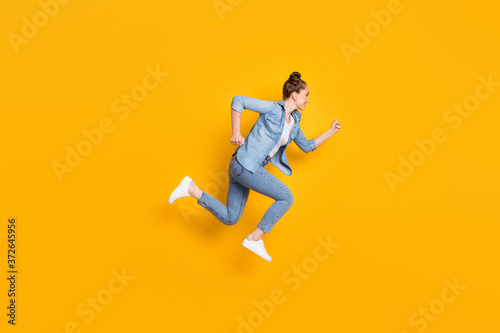 Full body profile photo of attractive teen lady jumping high up running race marathon excited to win rushing wear casual denim shirt sneakers pants isolated yellow color background