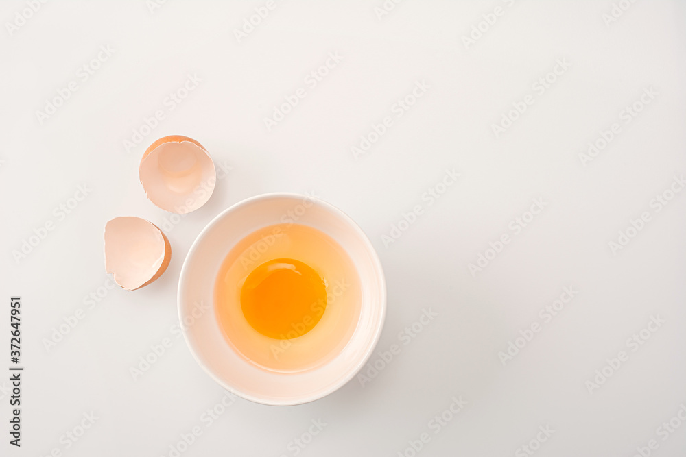 Beautyful brown chicken egg is half broken with yolk. Raw uncooked egg in white bowl on white kitchen table background. Beautyful brown chicken egg is half broken with yolk. Raw uncooked egg in white bowl on white kitchen table background.