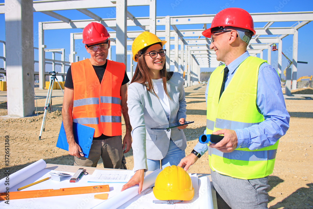 Female architect, construction engineer and manager talking about the project on construction site. Teamwork - group of builders and architect in hardhats, positive emotions, joy and smiles Female architect, construction engineer and manager talking about the project on construction site. Teamwork - group of builders and architect in hardhats, positive emotions, joy and smiles