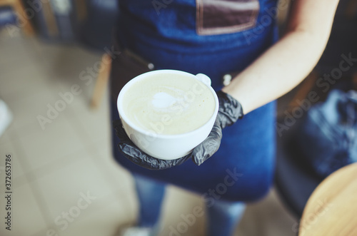 Barista wearing medical latex black gloves, making cappuccino, bartender preparing coffee drink. Blurred image, selective focus