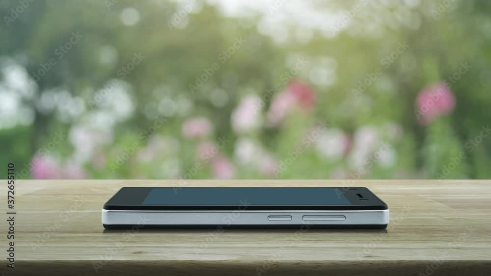 Shopping cart flat icon on modern smart mobile phone screen on wooden table over blur pink flower and tree in park, Business shop online concept