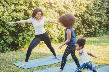 Black African American mom with child playing yoga family activity together at backyard during self quarantine at home.