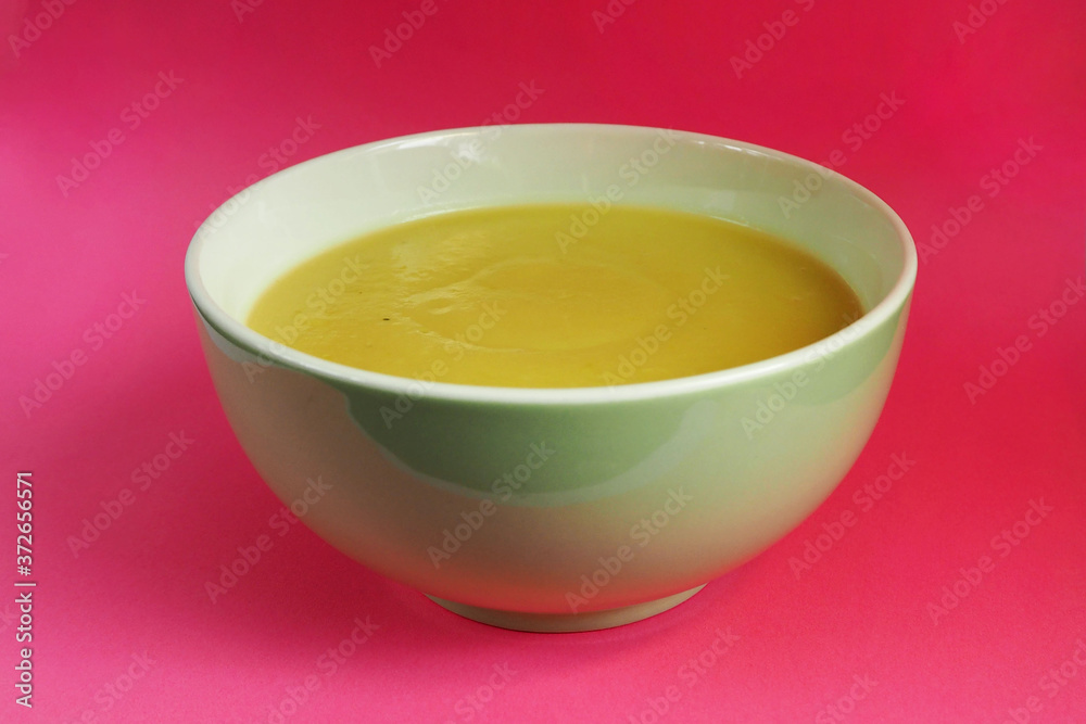 green plate with cream soup of zucchini, potatoes, cream, onions on a pink background side view . cooking gluten-free food at home green plate with cream soup of zucchini, potatoes, cream, onions on a pink background side view . cooking gluten-free food at home