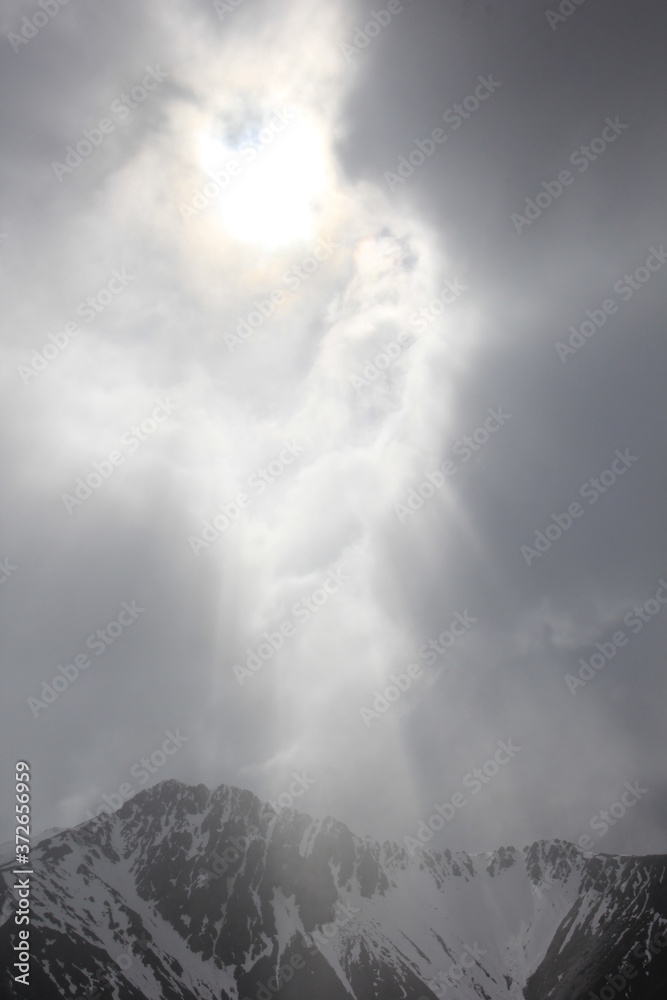 曇天の隙間から射す日光が雪山を照らす風景