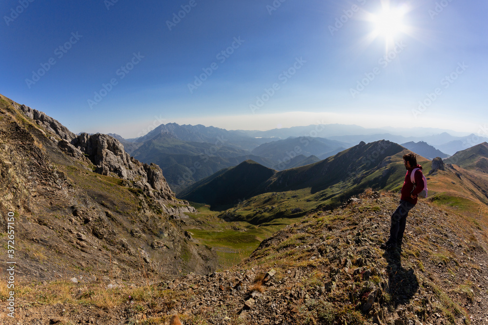 Man observing mountainous landscape from the top of a mountain in the top of mountain Coriscao in Leon, Asturias, Spain