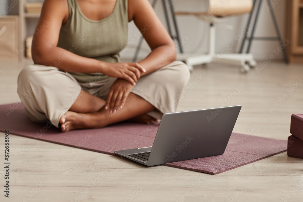 Naklejka premium Close-up of woman sitting on exercise mat in front of laptop and watching yoga exercises online at home